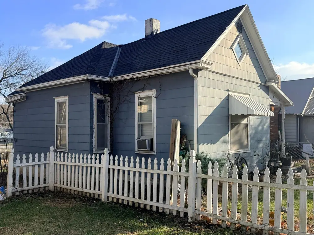 Blue clapboard house with a new dark asphalt shingle roof behind a white picket fence