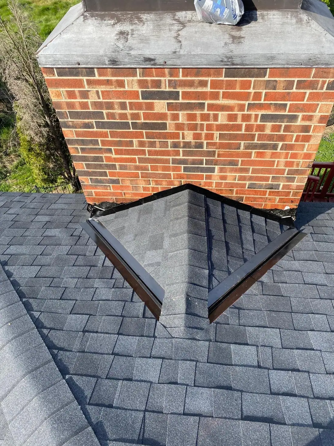 New shingles and a metal cricket flashed around a brick chimney