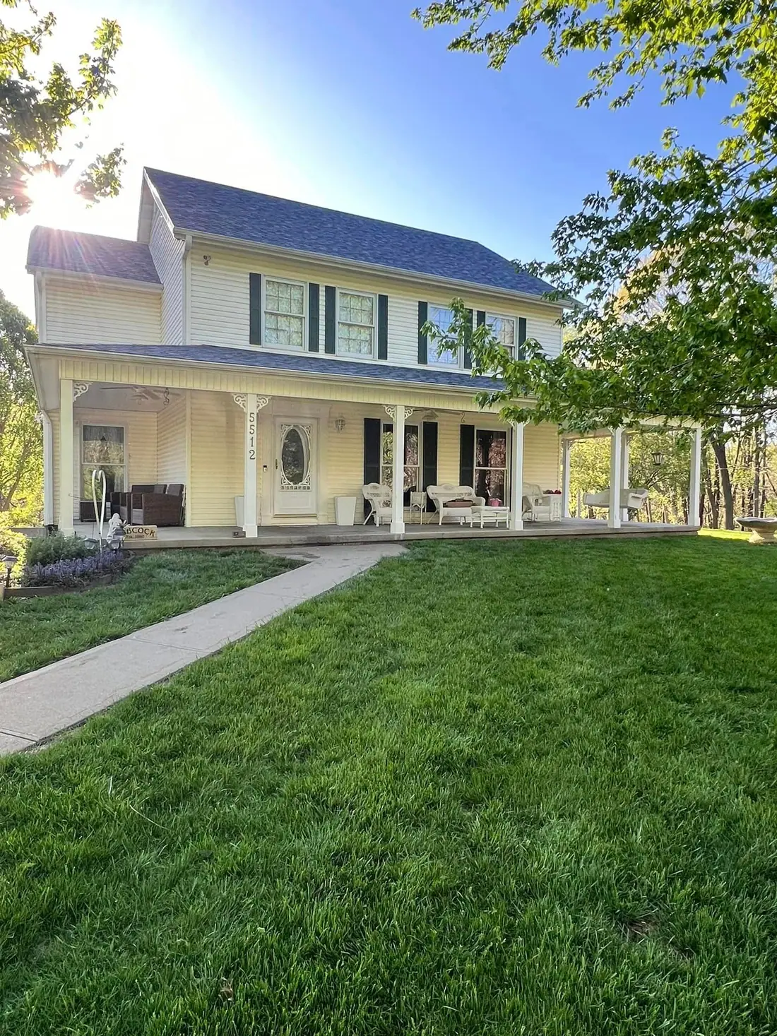 Two-story farmhouse with a wraparound porch and a new roof in afternoon sun
