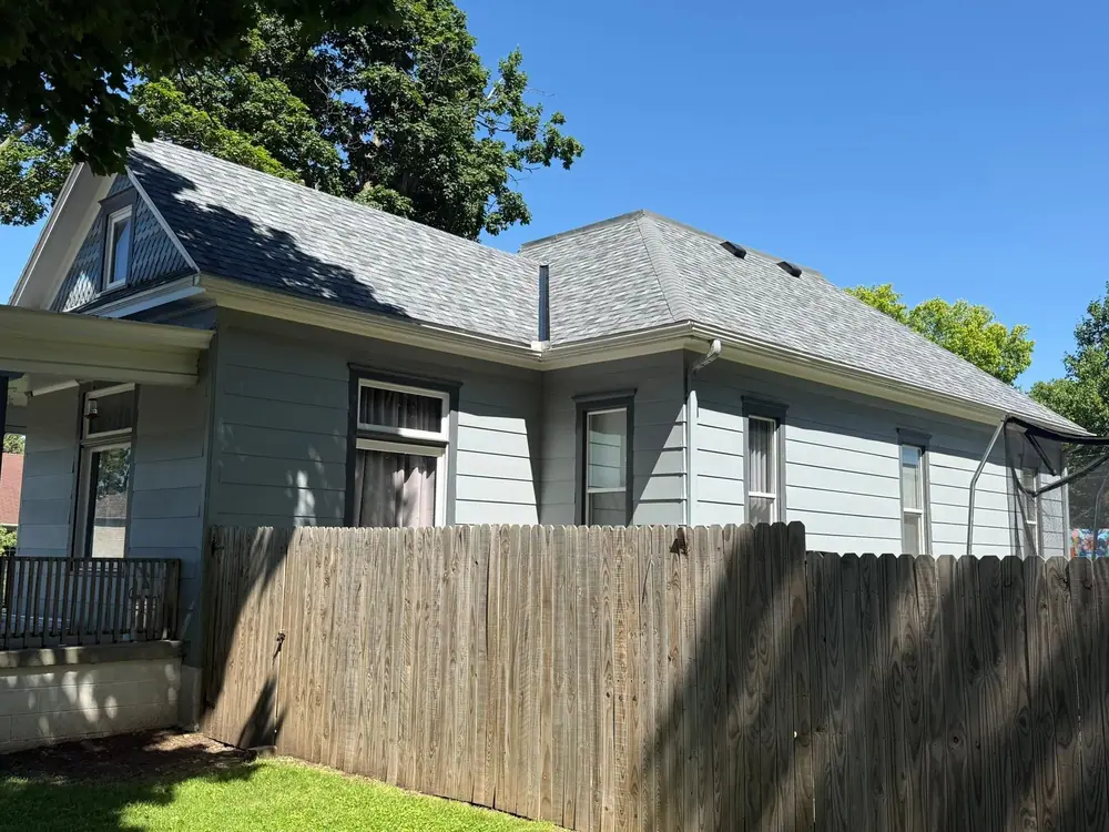 Gray house with a new roof, fresh flashing and a wood privacy fence
