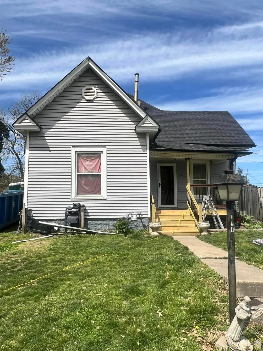 Gray vinyl-sided house with a new black shingle roof and a dumpster at the curb