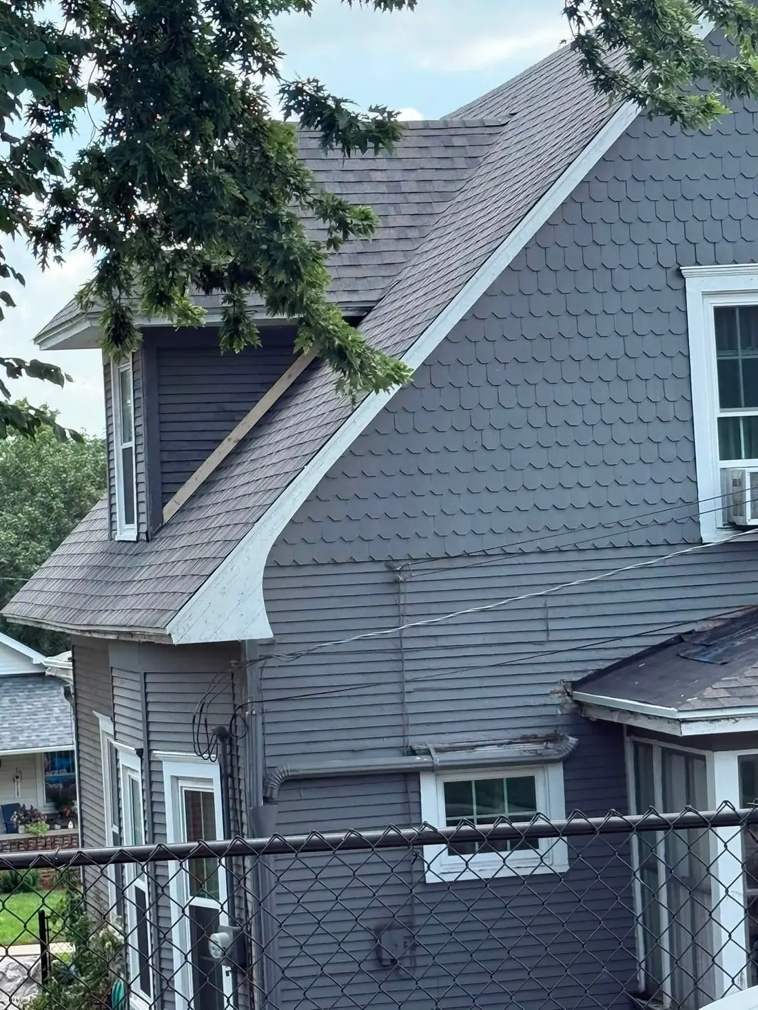 Gray house with scalloped gable siding under a new shingle roof