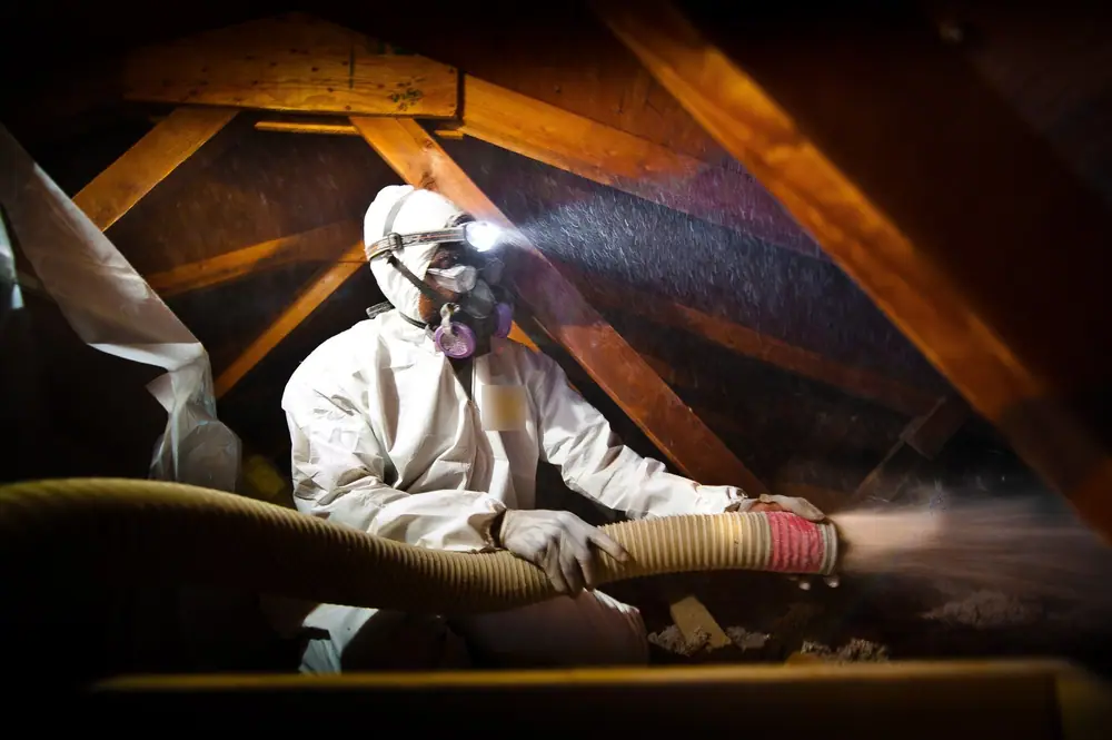 Installer blowing loose-fill insulation into an attic between the trusses