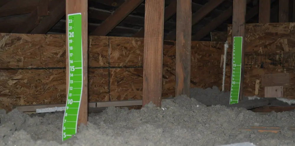 Insulation depth rulers stapled to attic framing over blown-in insulation