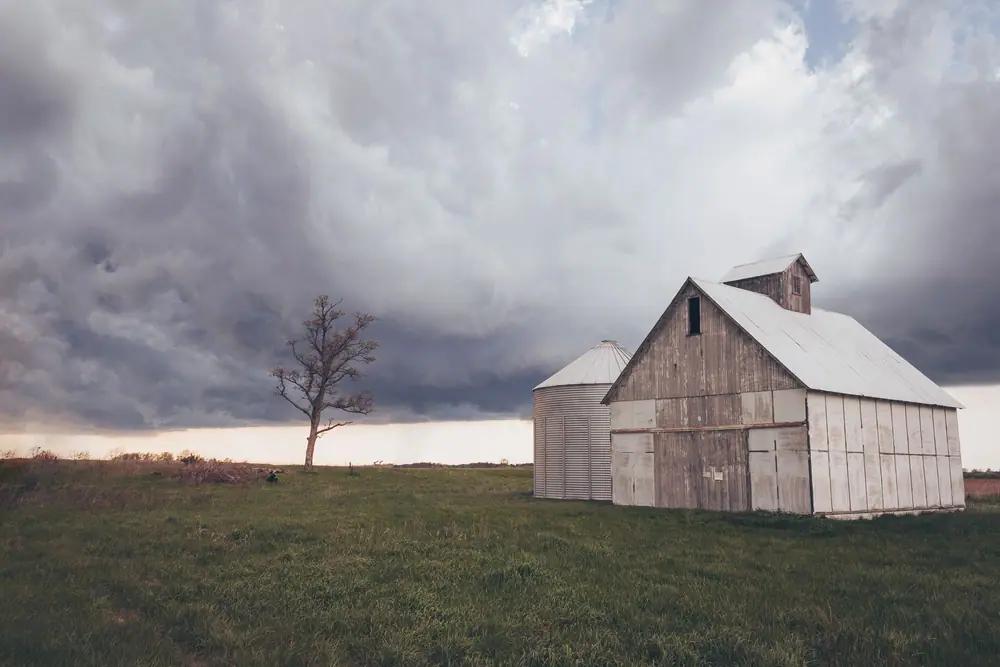 White barn and grain bin under dark storm clouds in farm country