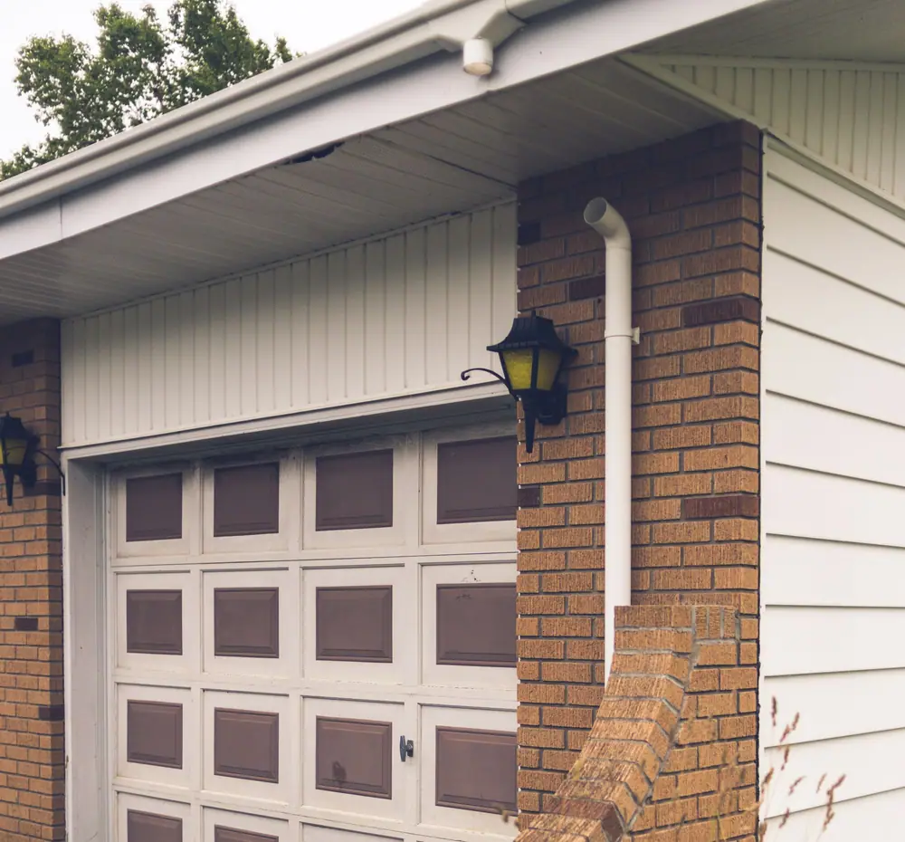 White gutter, soffit and downspout with elbow beside a brick garage pier