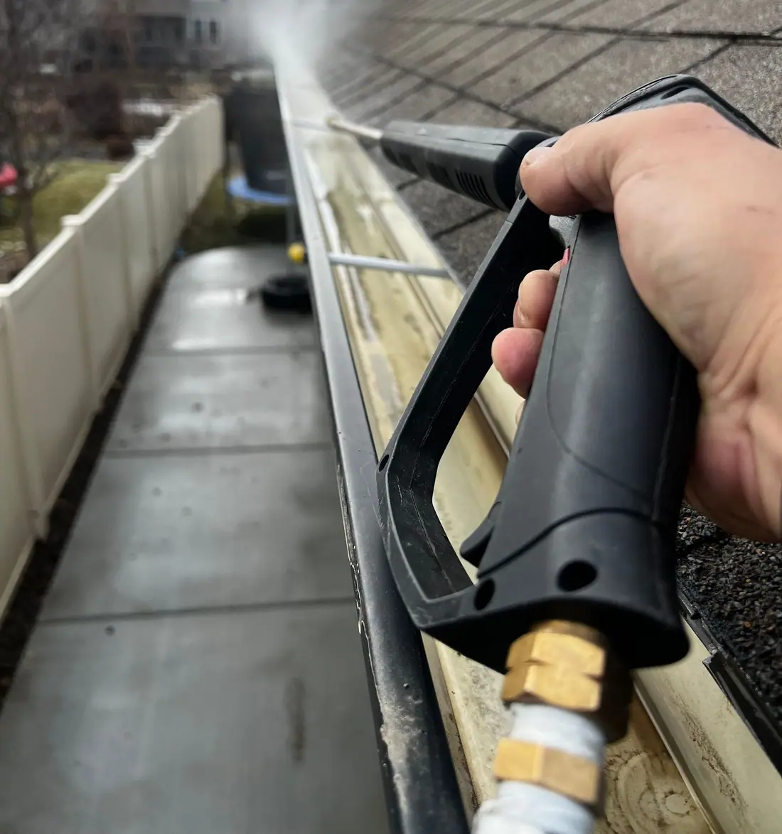 Gutter being flushed clean with a water wand along a shingle roof edge
