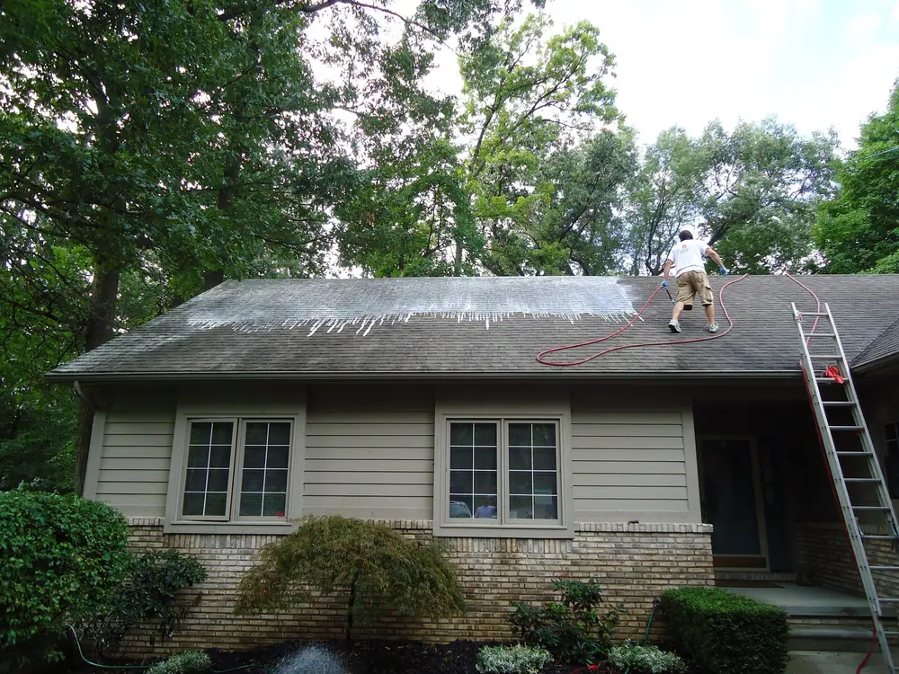 Worker washing dark algae streaks off an asphalt shingle roof