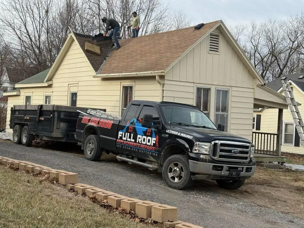 Full Roof crew tearing off a roof while the company pickup and dump trailer wait in the driveway