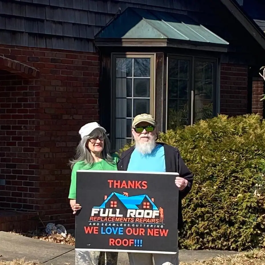 Homeowners in front of their brick house holding a Full Roof sign that reads “We love our new roof”